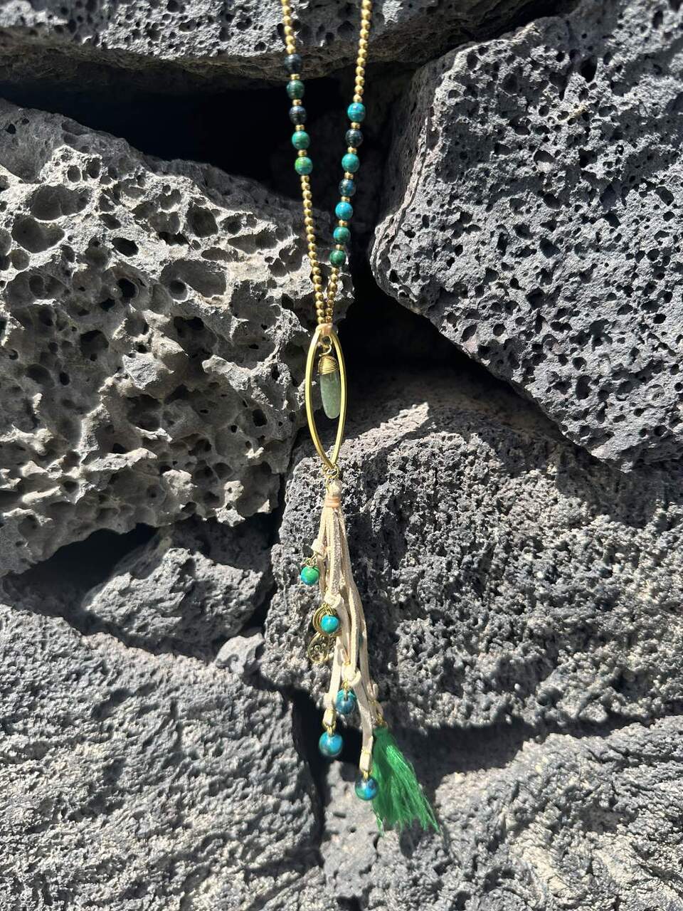 Collar largo de cuero y cuentas en verde con colgante ovalado y piedra rematado con abalorios en dorado y piedras y borla de hilo