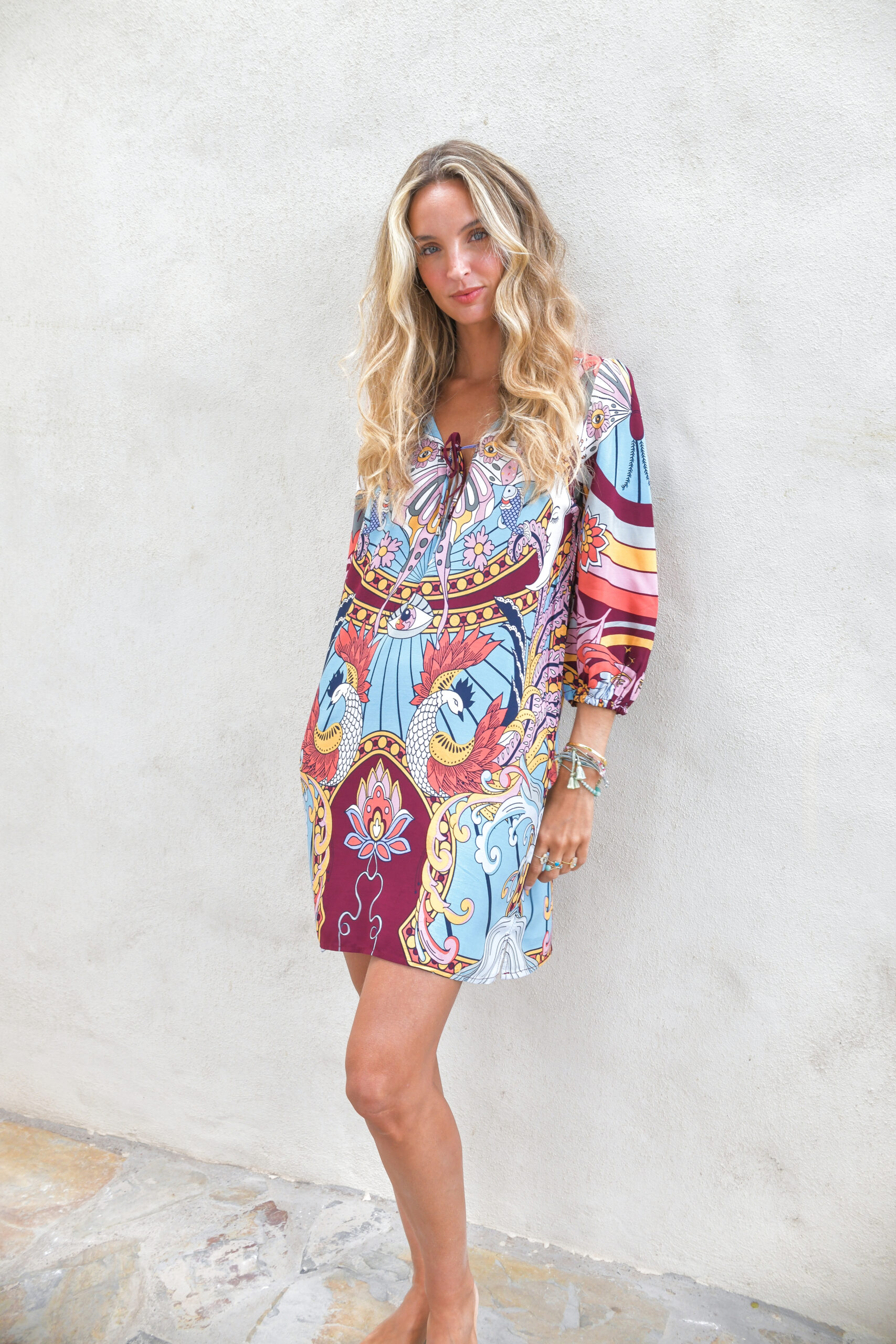 Vestido Mini Boho corte recto escote en V con lazo delantero manga 3/4 con puños elásticos y dobladillo con ribete de pon pon estampado estampado multicolor de pavos reales flores y motivos místicos en una vibrante paleta de turquesas, granate y dorados Neandnu