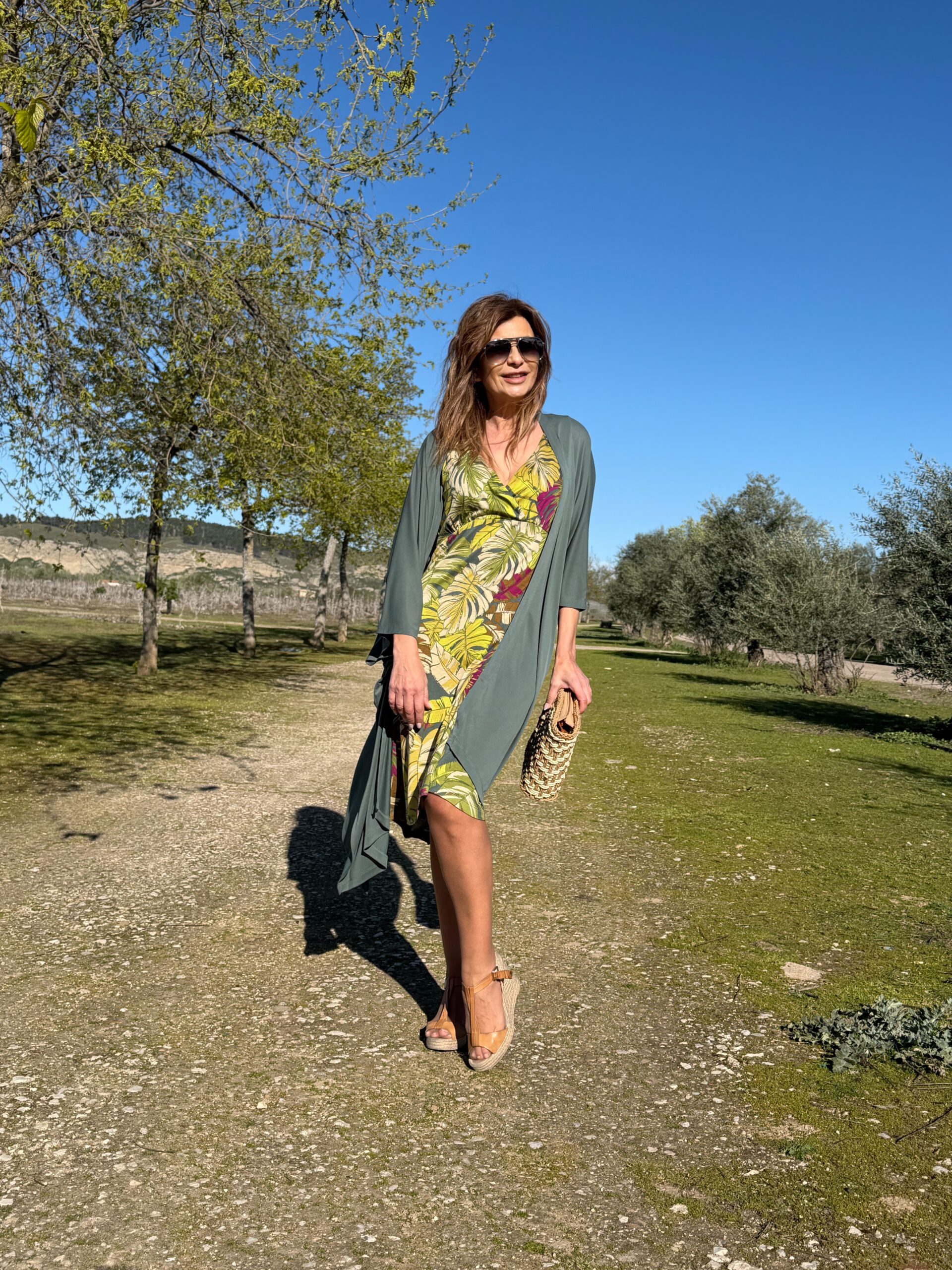 Vestido de tirante ancho largo a la rodilla escote en V efecto cruzado y espalda escotada en pico cintura entallada y falda acampanada estampado de hojas multicolor sobre fondo verde Neandnu
