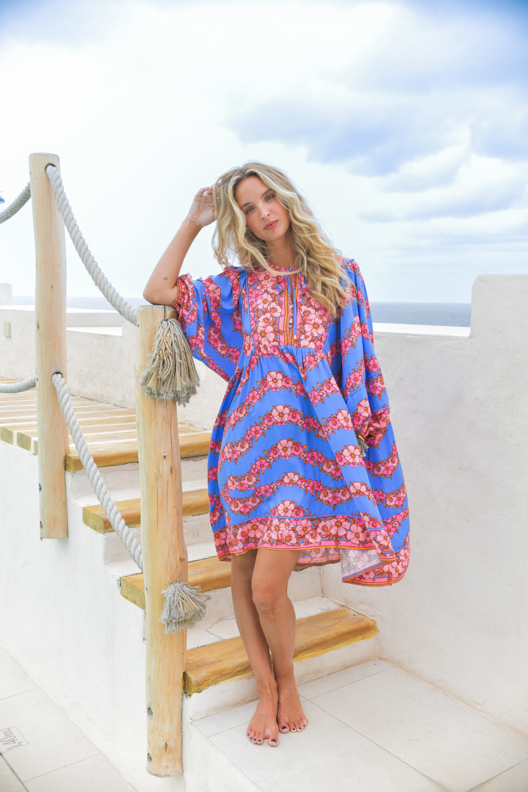 vestido mini boho estampado floral tonos rojos rosas y naranjas sobre fondo azul oversize escote V con botones en la zona del pecho y bolsillos que le dan forma detalles de encaje mangas globo con puño elástico Neandnu