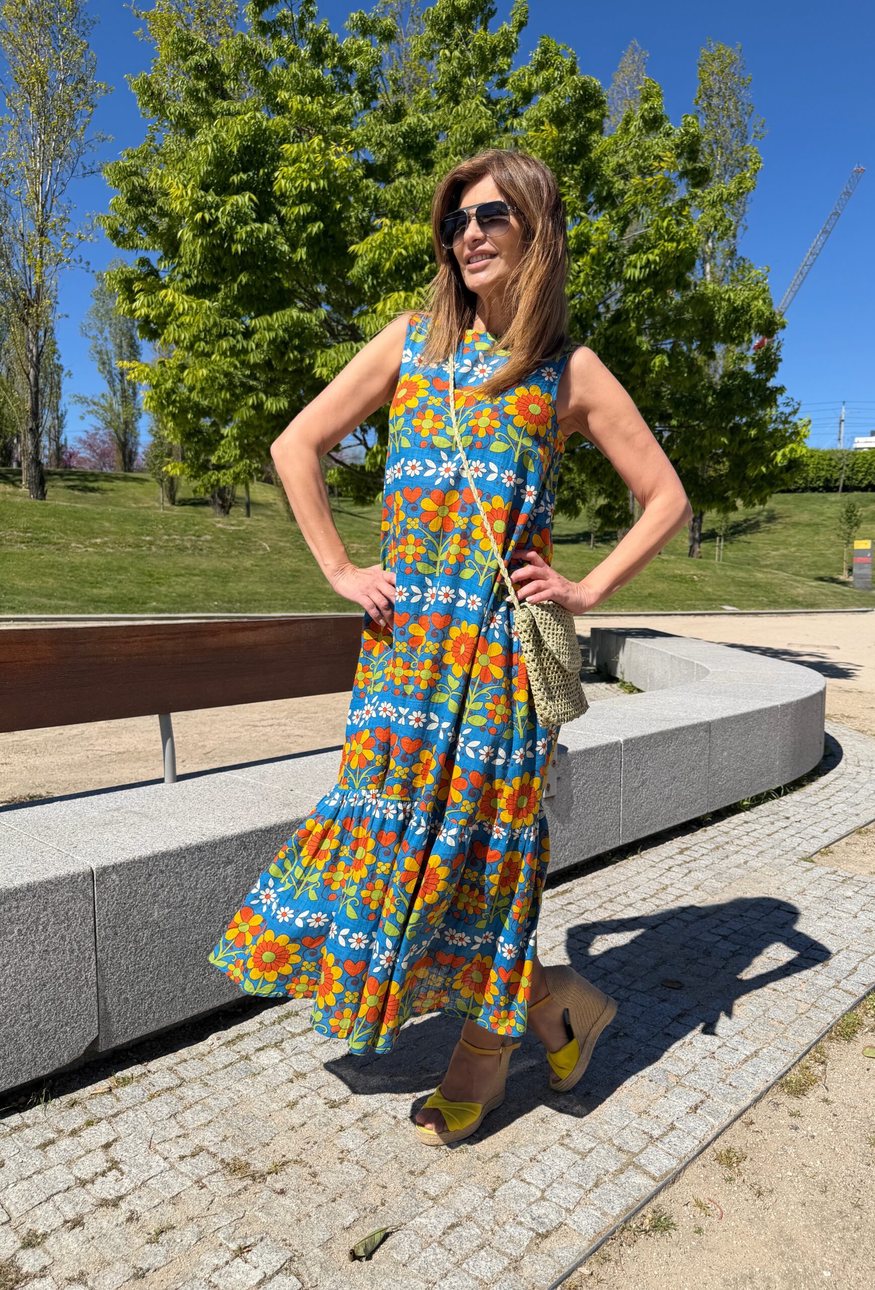 Vestido maxi sin mangas en un estampado floral multicolor sobre fondo azul cuello redondo bolsillos laterales y detalle de pliegues en la falda Neandnu